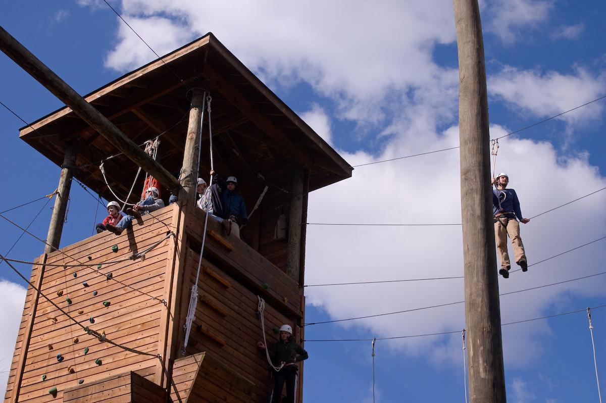 在newbb电子平台，学生们坐在岩壁上的高绳索课程塔上